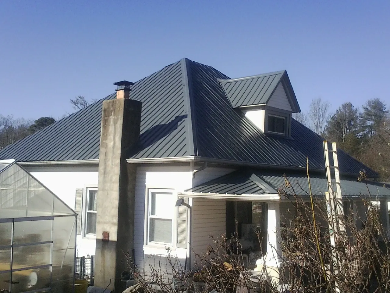 Dark blue standing seam metal roof on a white farmhouse with dormer — Slate & Tile Roof Repair by Roofing Brothers in Perry