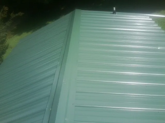 New green metal panels meeting at the ridge of a roof — Flat Roof Repair work by our crew in Perry