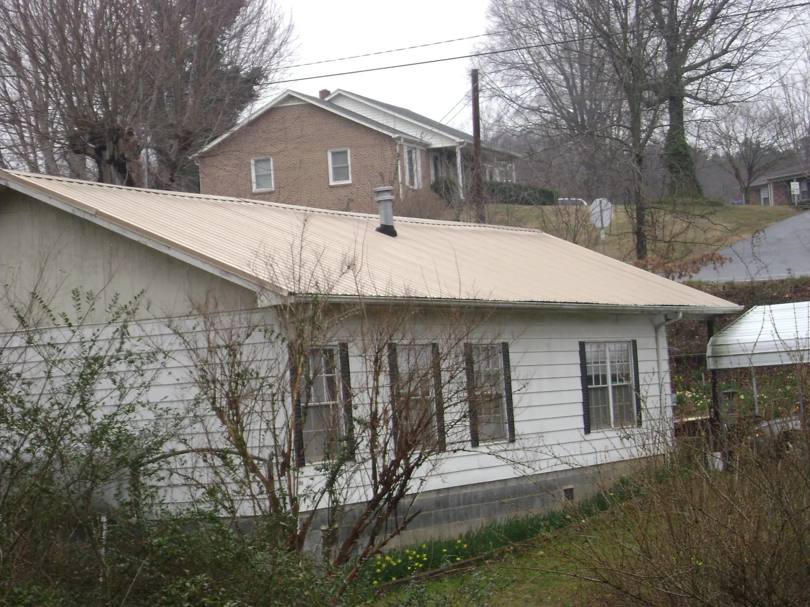 Tan metal roof on a white sided house set into a hillside — Commercial Roofing by Roofing Brothers in Perry