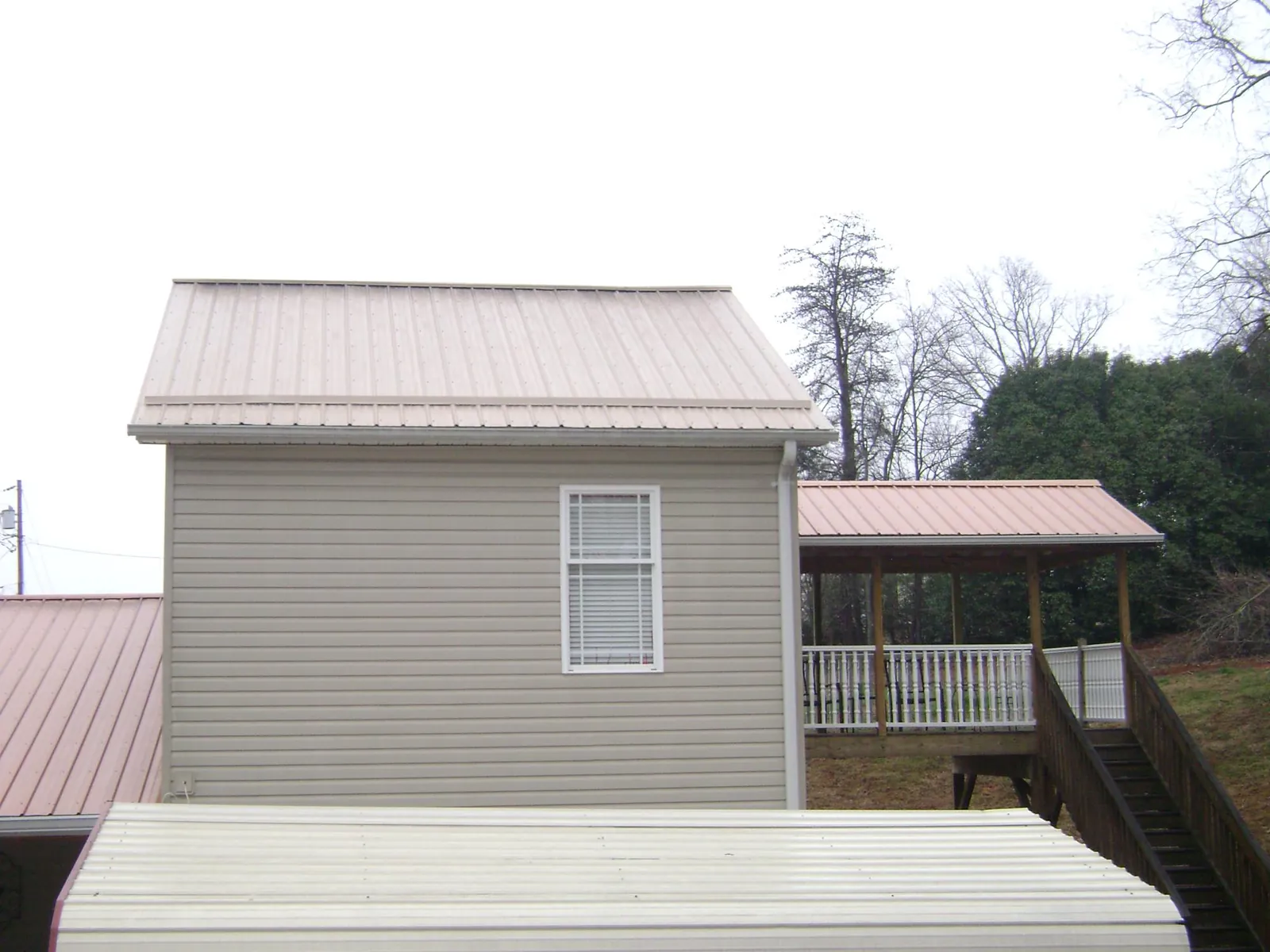 Tan metal roofs on a two story addition and attached porch, from a Roof Replacement job in Perry